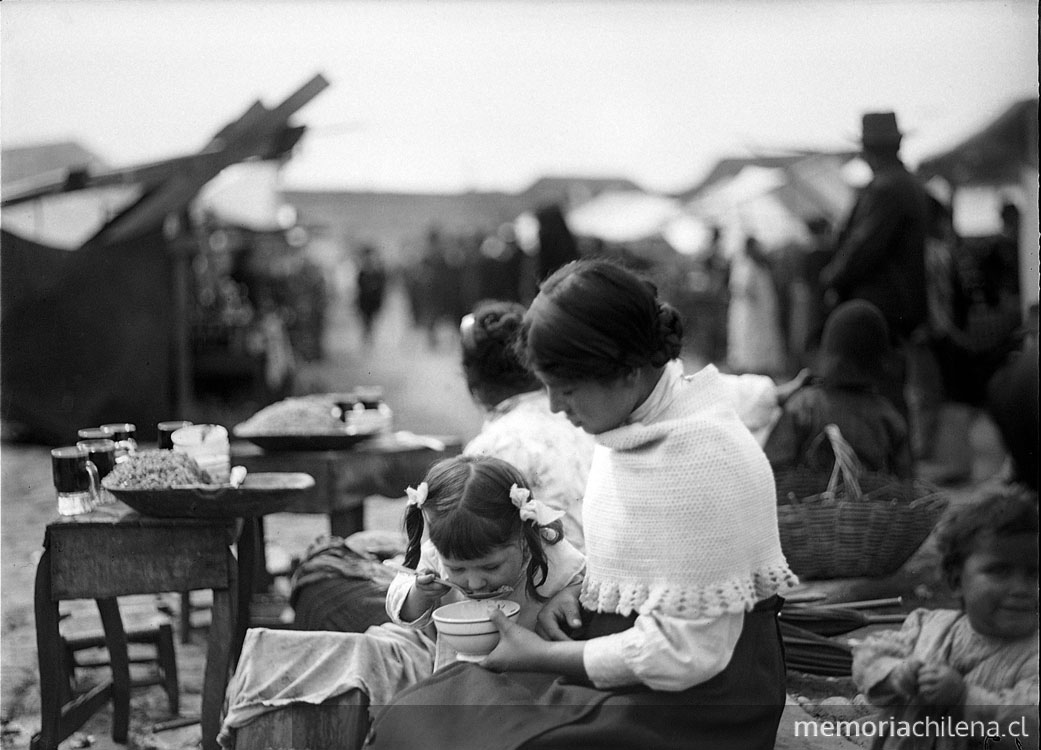 Joven mujer alimentando a una de sus hijas pequeñas en su puesto en la feria
