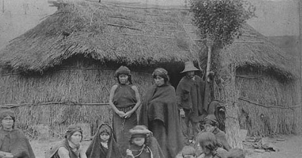 Grupo mapuche junto a un rewe, frente a su ruka