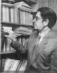 Mario Orellana junto a repisa consultando libros
