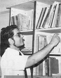 Mario Orellana junto a repisa consultando libros
