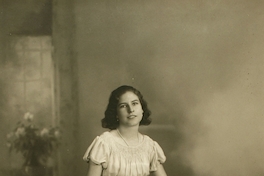 Mujer joven sentada sobre un baúl con un vestido hasta el suelo amplio y acinturado, entre 1928 y 1930