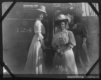 Cuatro señoras, con sombreros, posan en la escalera del tren, portan sombrillas