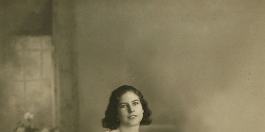 Mujer joven sentada sobre un baúl con un vestido hasta el suelo amplio y acinturado, entre 1928 y 1930